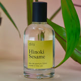 The Hinoki Sesame 50ml Unisex Eau de Parfum on a pink background with leaves.
