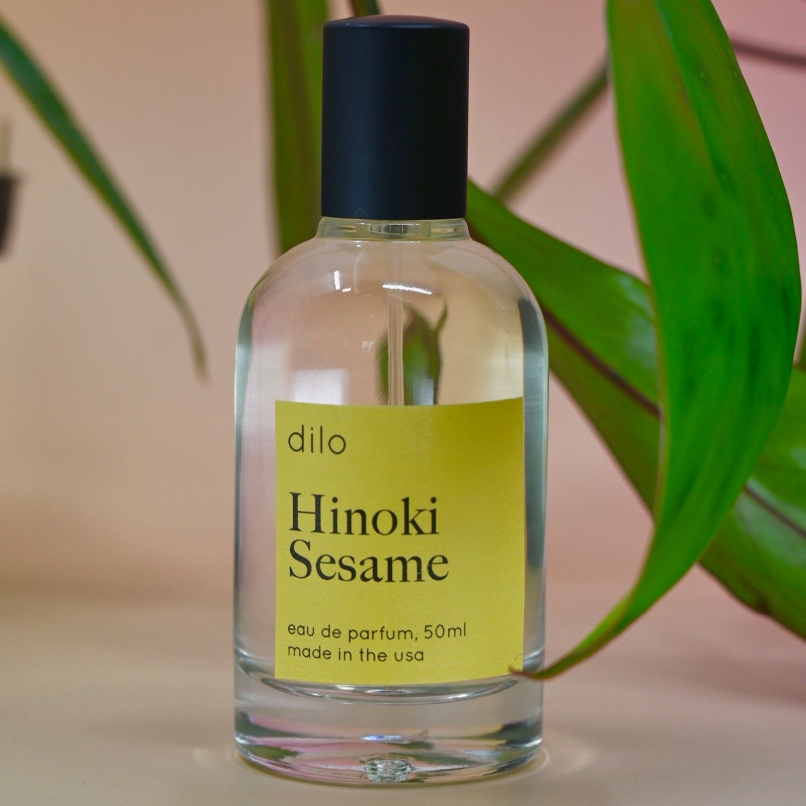 The Hinoki Sesame 50ml Unisex Eau de Parfum on a pink background with leaves.
