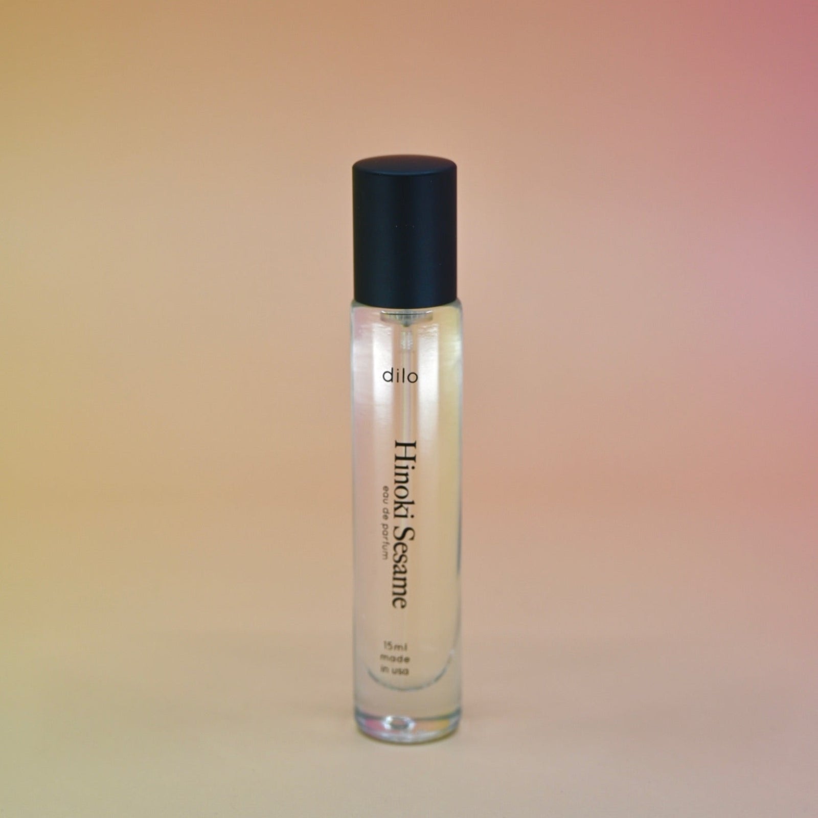 The Hinoki Sesame 5ml Unisex Eau de Parfum Travel Sprayer on a pink and yellow background.
