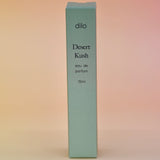 The box of the Desert Kush 15ml Unisex Eau de Parfum Travel Sprayer on alight pink background.