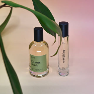 The Desert Kush 15ml Unisex Eau de Parfum Travel Sprayer and regular sized bottle on a light pink background with leaves.