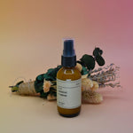 The No. 05 Coconut + Vetiver Room Spray in front of a dried flower bundle on a pink background.