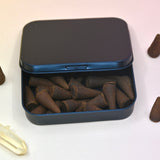 The inside of the dilo incense cone container surrounded by incense cones and a crystal all on a light pink background.