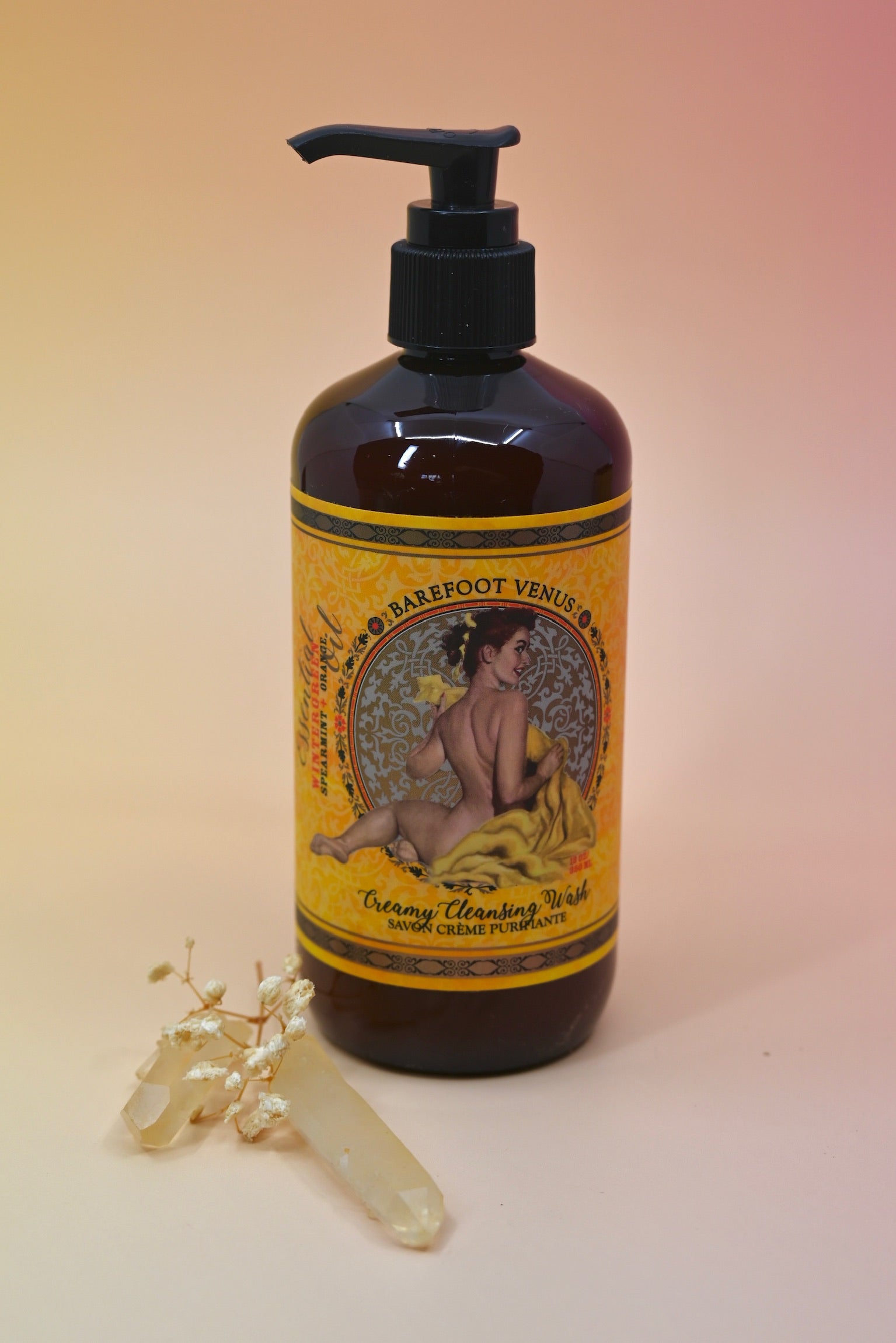 The Essential Oil Cleansing Hand & Body Wash with a crystal in front of it on a light pink background.