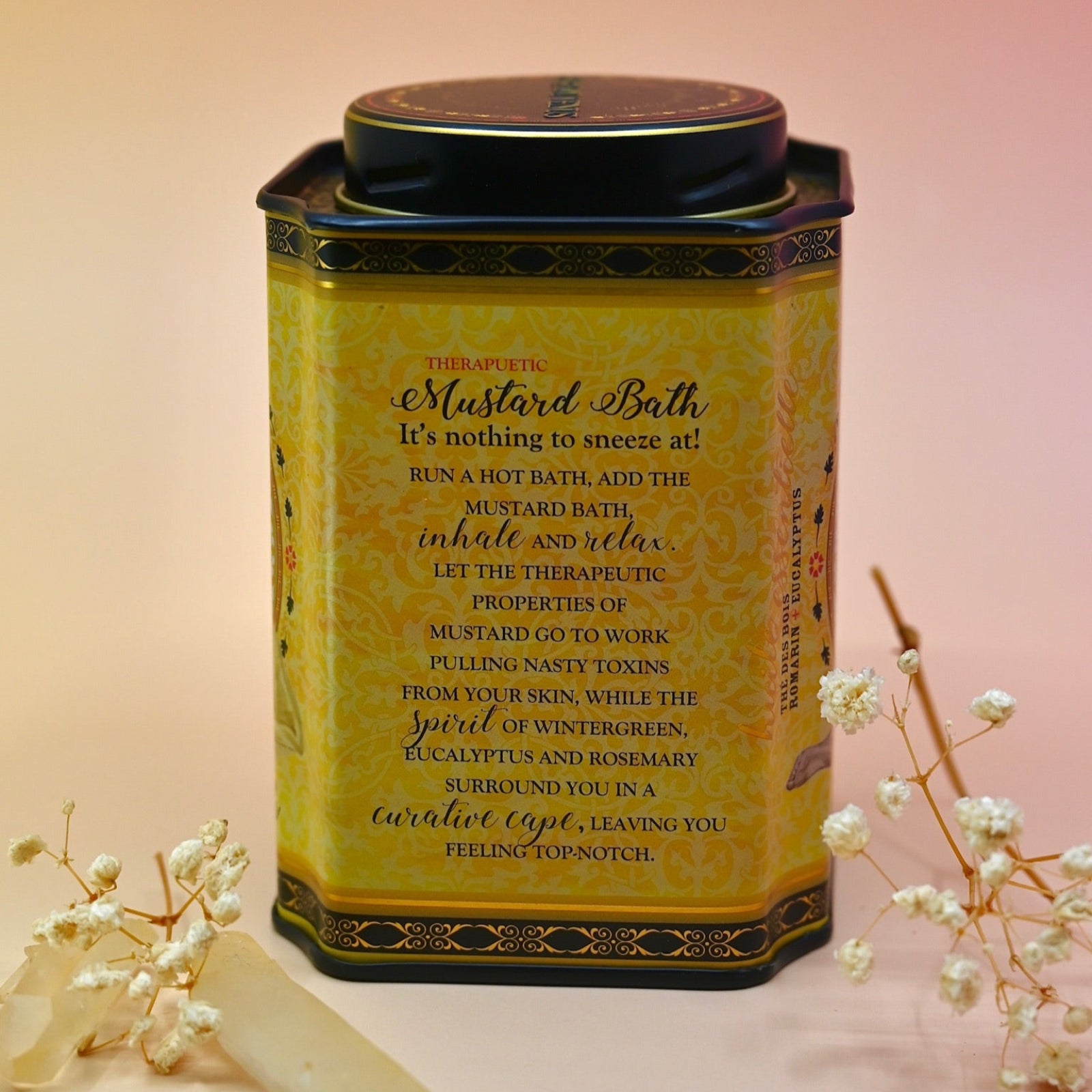 The back of the 100% Natural Mustard Bath Soak with a crystal and dried flowers in front of it on a light pink background.