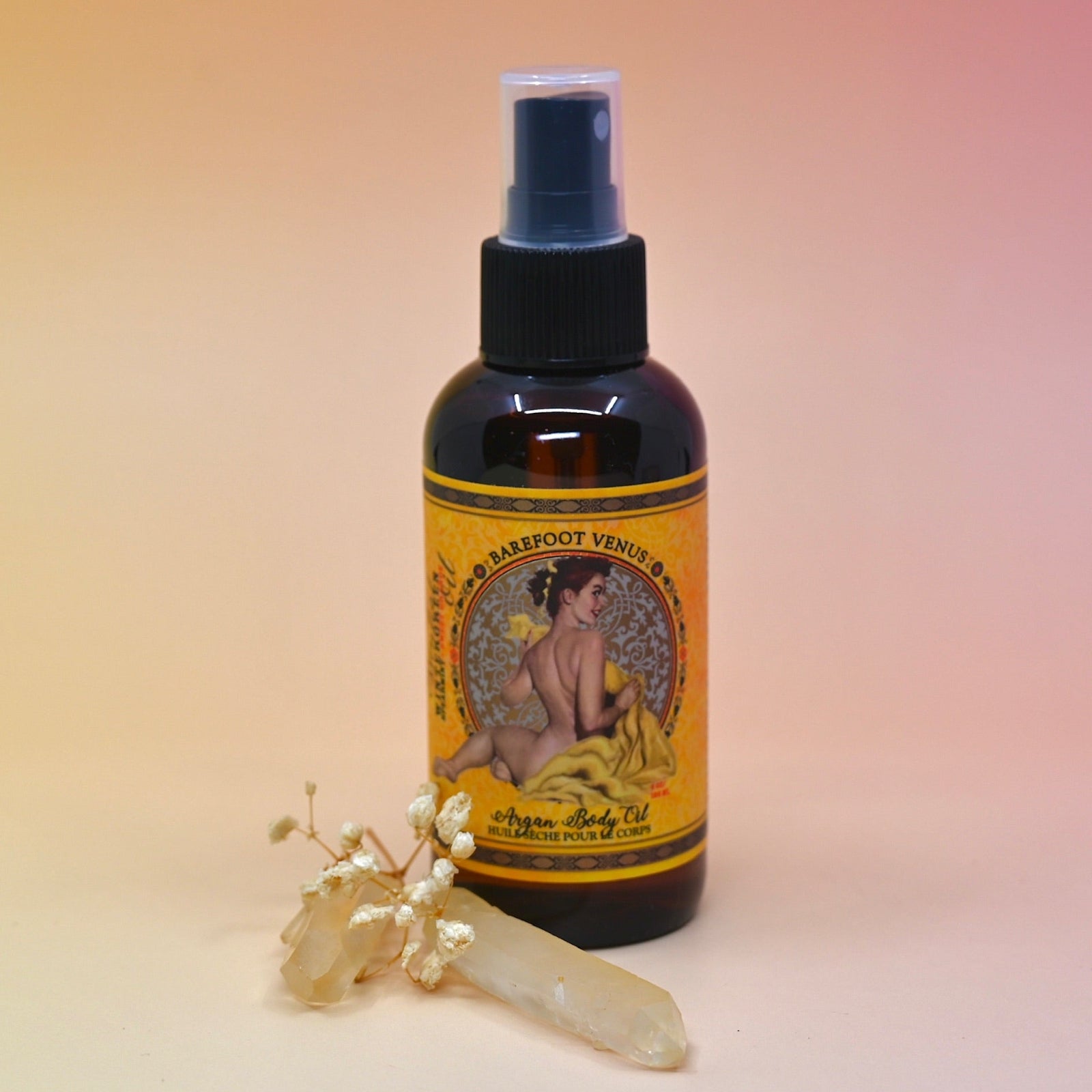 The Essential Oil Argan Body Oil with a crystal in front of it on a pink background.