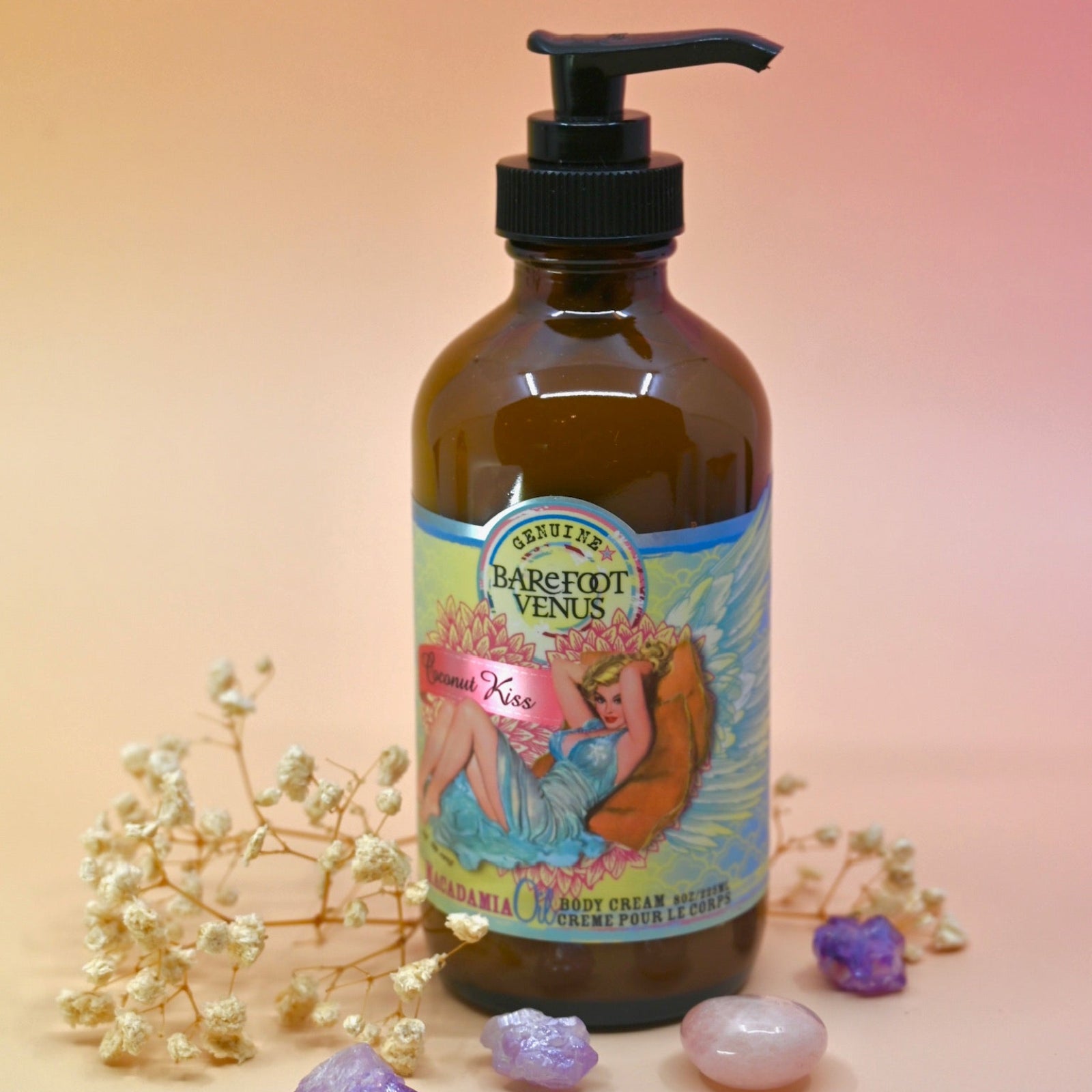 The Coconut Kiss Body Cream Moisturizer surrounded by crystals and dried flowers on a pink background.