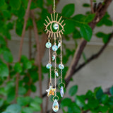 The evil eye  Fairy Lights Suncatcher in front of a cream-colored brick wall with greenery.