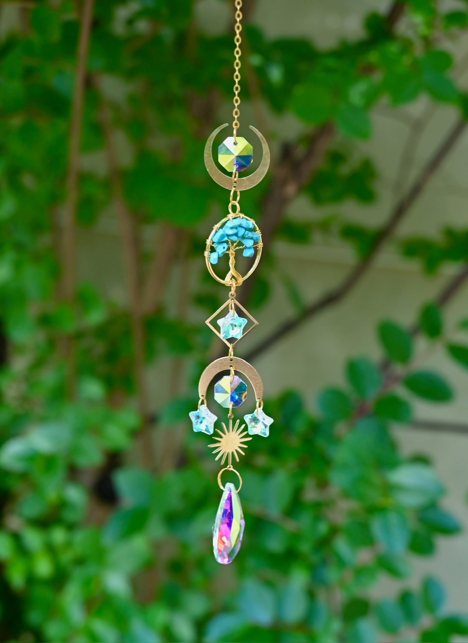 The turquoise Tree of Life Crystal Suncatcher with greenery in the background.