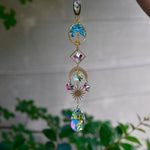 The turquoise Tree of Life Crystal Suncatcher with greenery in the background.