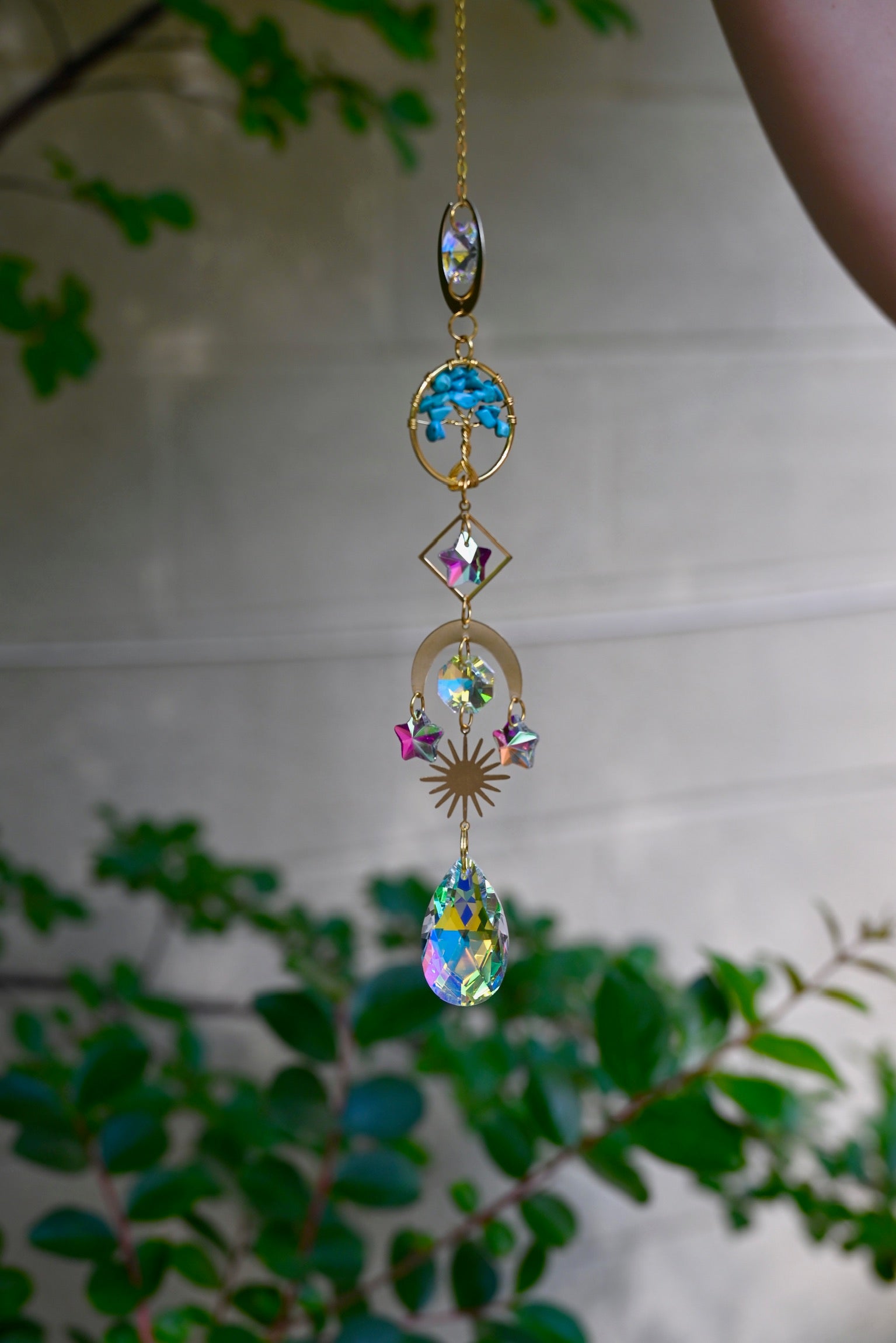 The turquoise Tree of Life Crystal Suncatcher with greenery in the background.