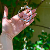 The Aquamarine Gemstone Suncatcher in front of a cream-colored brick wall and greenery.
