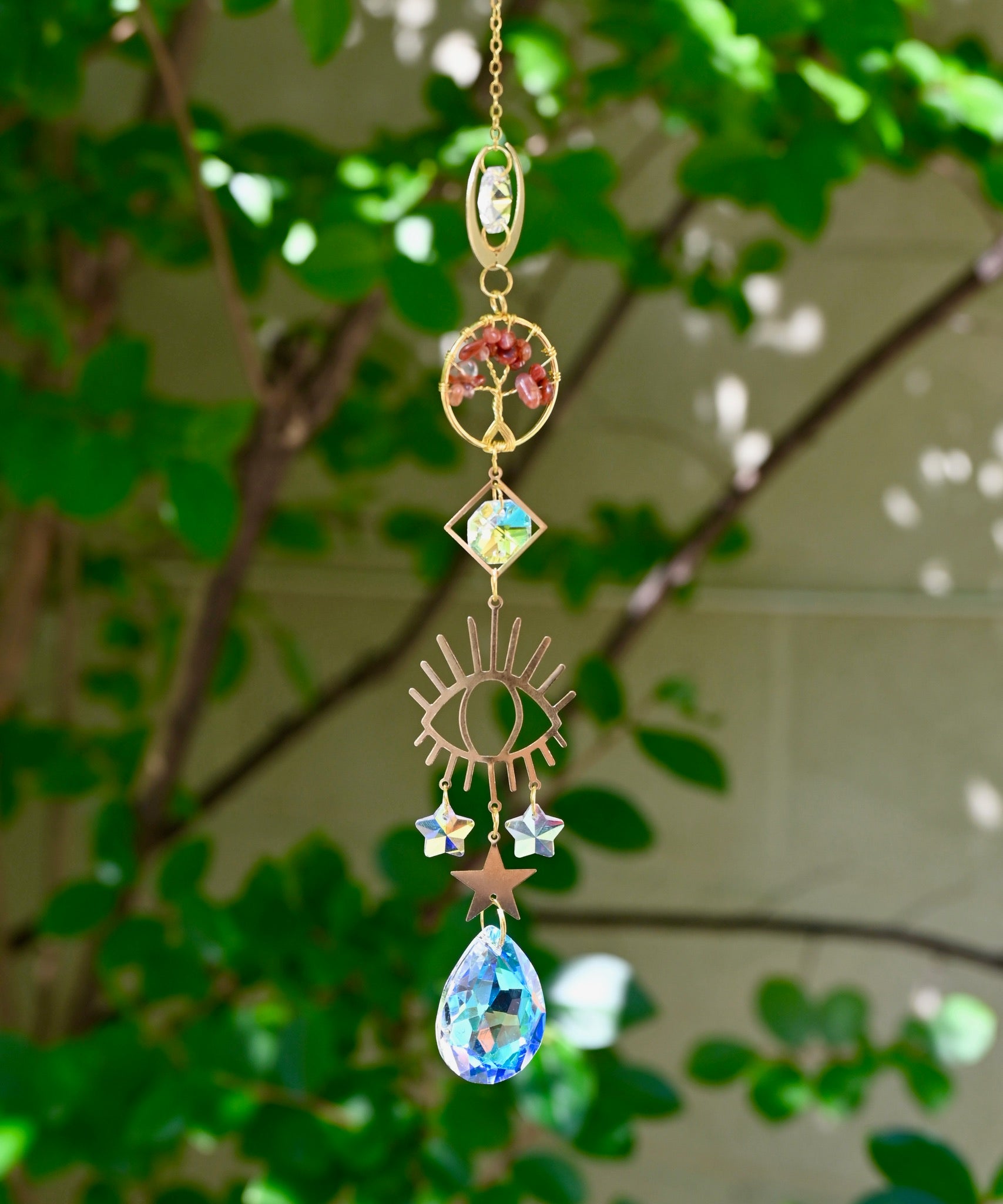 The carnelian Tree of Life Crystal Suncatcher with greenery in the background.