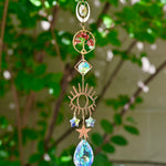The carnelian Tree of Life Crystal Suncatcher with greenery in the background.