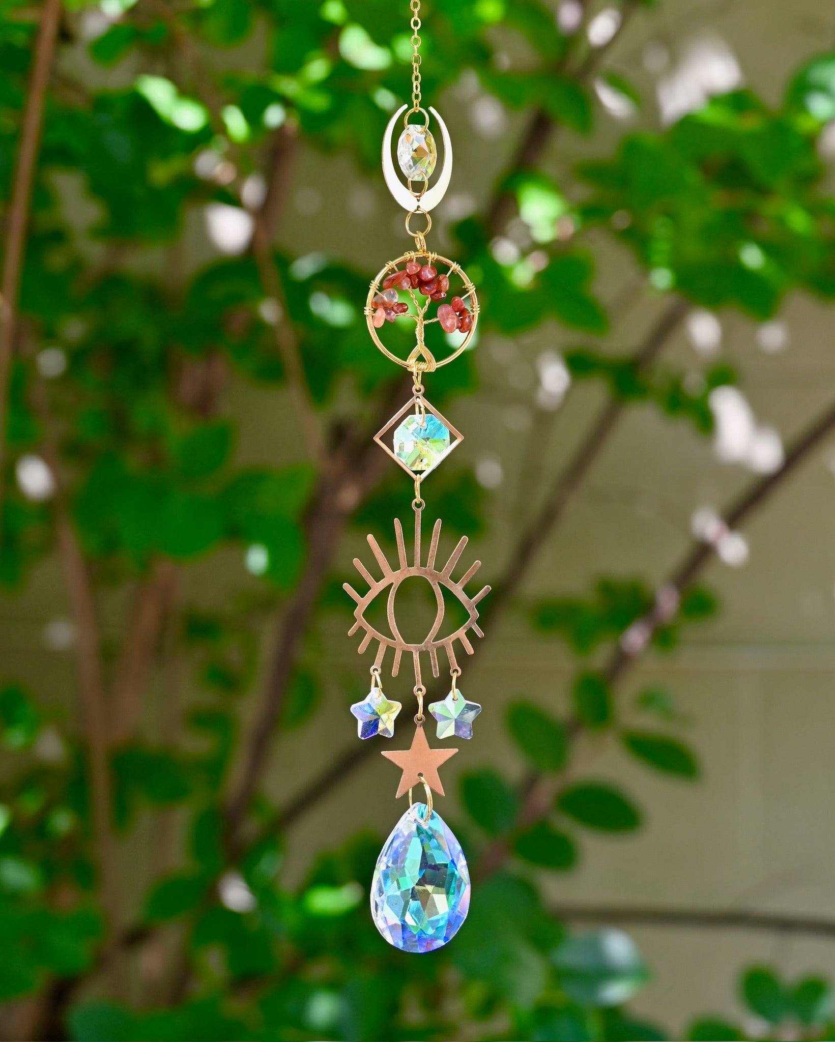 The carnelian Tree of Life Crystal Suncatcher with greenery in the background.