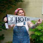The Hoth Pennant - Woolen Cotton Pennant being held in front of a cream-colored brick wall with greenery.