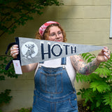 The Hoth Pennant - Woolen Cotton Pennant being held in front of a cream-colored brick wall with greenery.