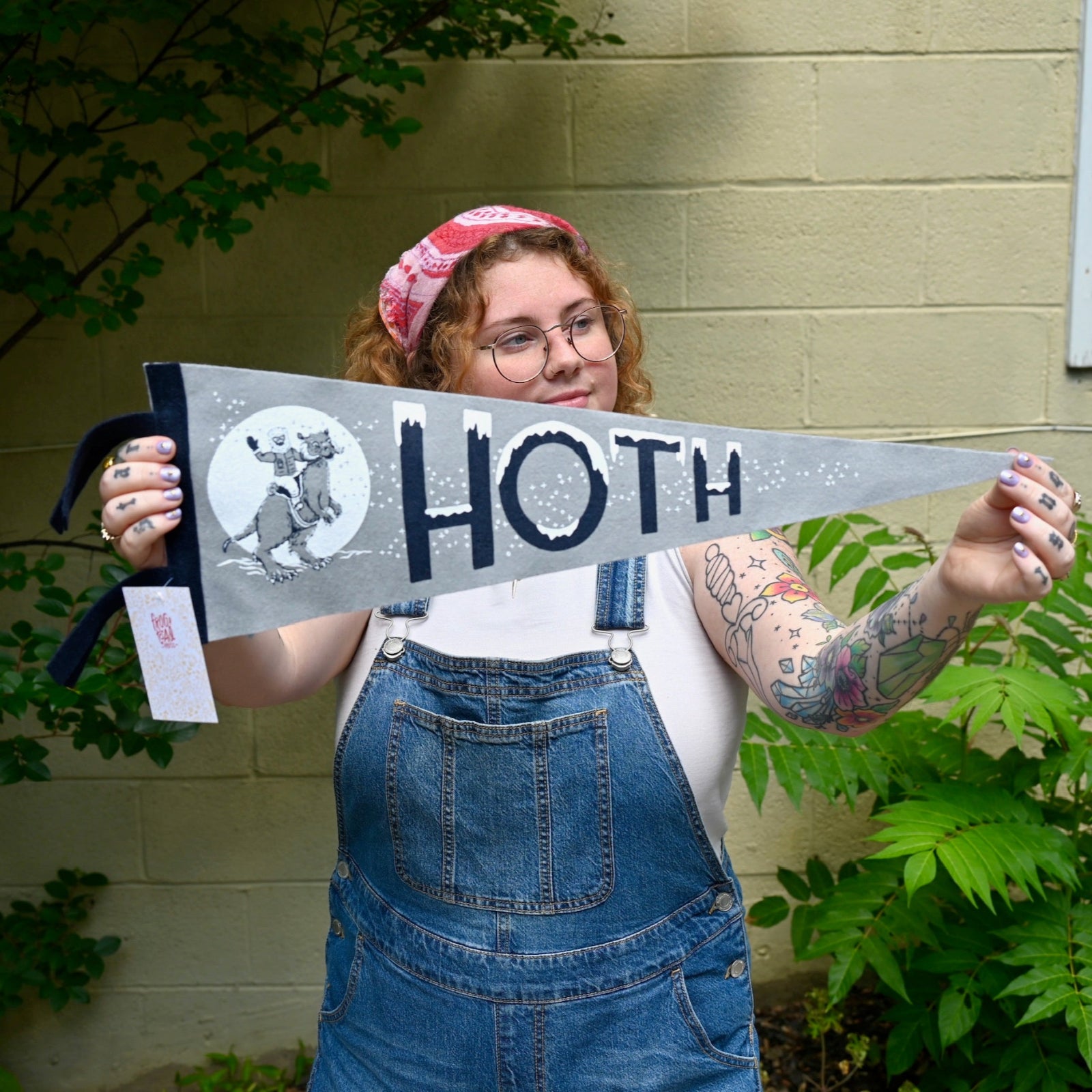 The Hoth Pennant - Woolen Cotton Pennant being held in front of a cream-colored brick wall with greenery.