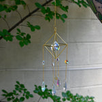 Someone holding the Gold Prism Sunlight Suncatcher in front of a cream-colored with greenery.