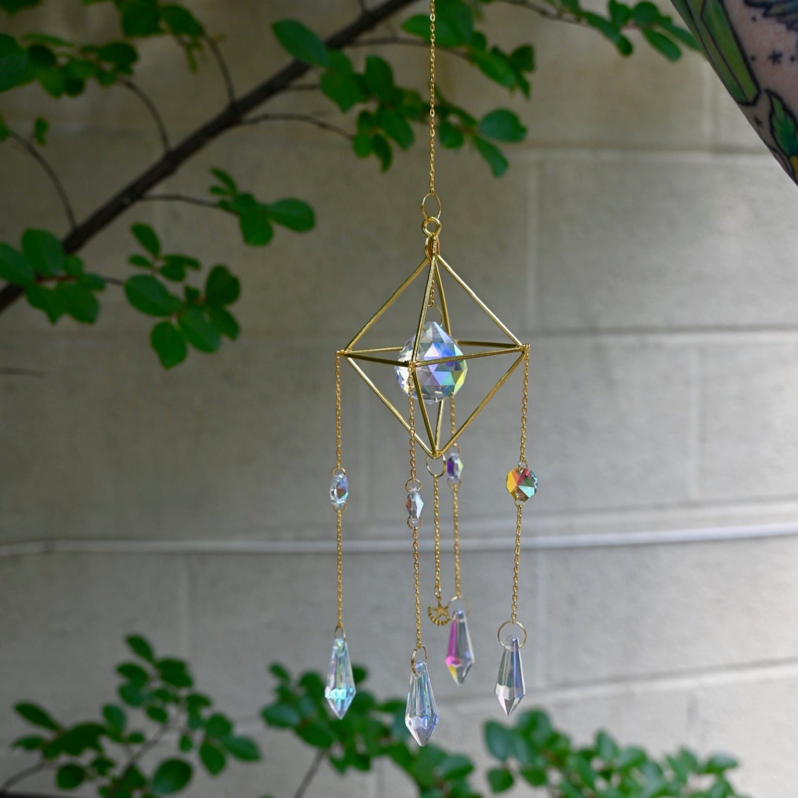 Someone holding the Gold Prism Sunlight Suncatcher in front of a cream-colored with greenery.