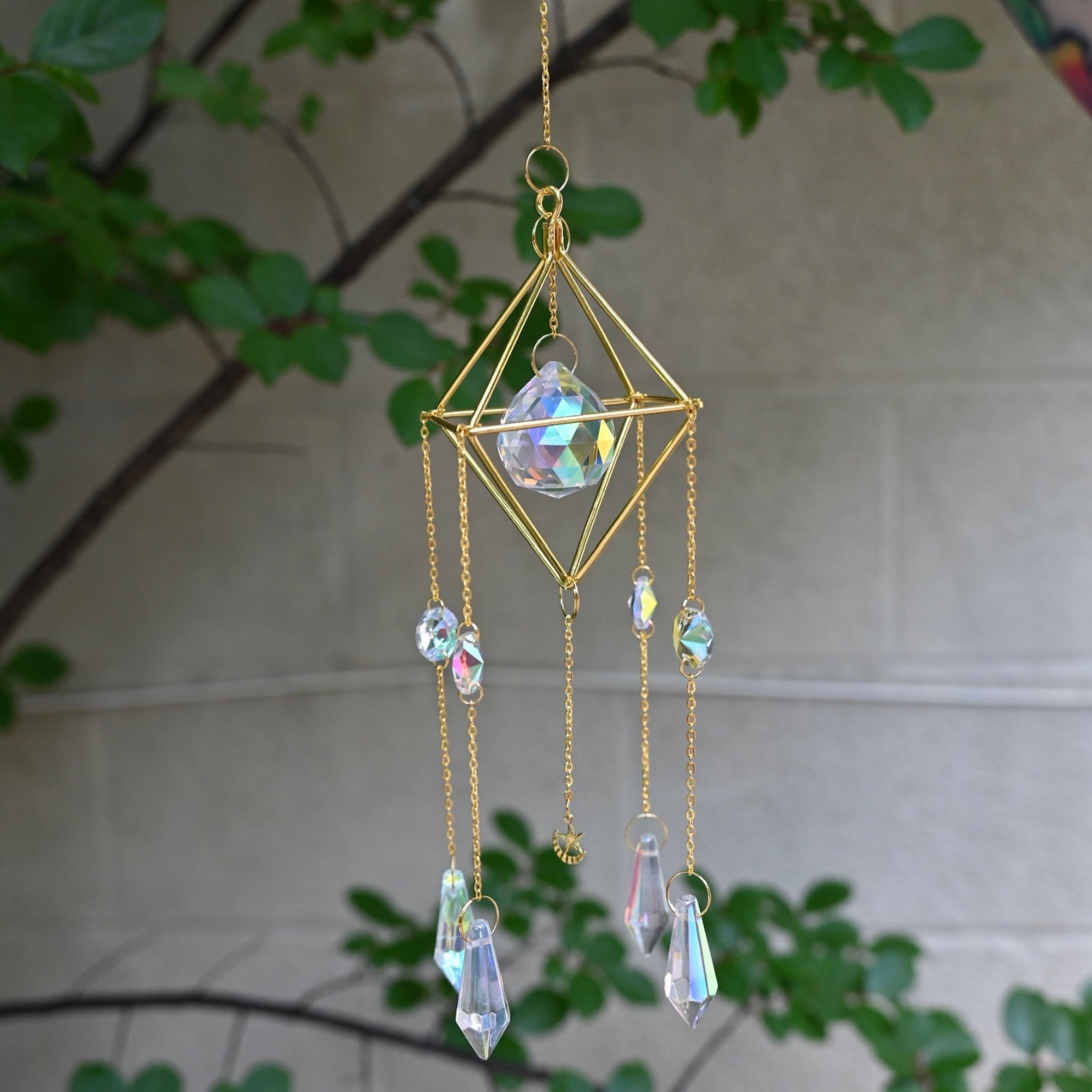 The Gold Prism Sunlight Suncatcher in front of a cream-colored with greenery.