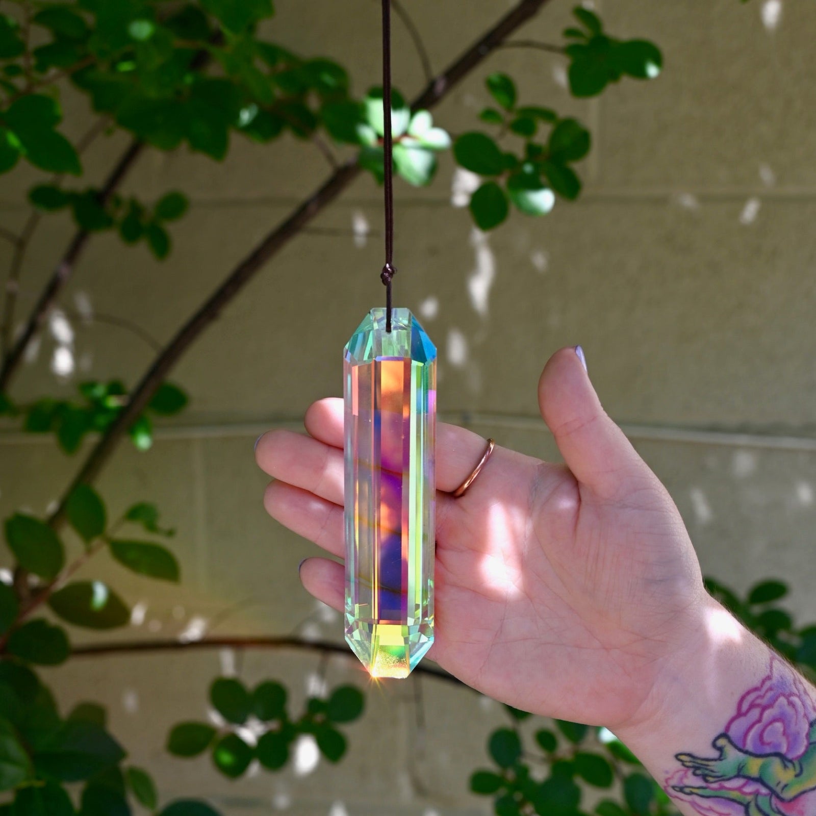 Someone holding the Prism Suncatcher in front of a cream-colored brick wall.