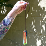 Someone holding the Prism Suncatcher in front of a cream-colored brick wall.