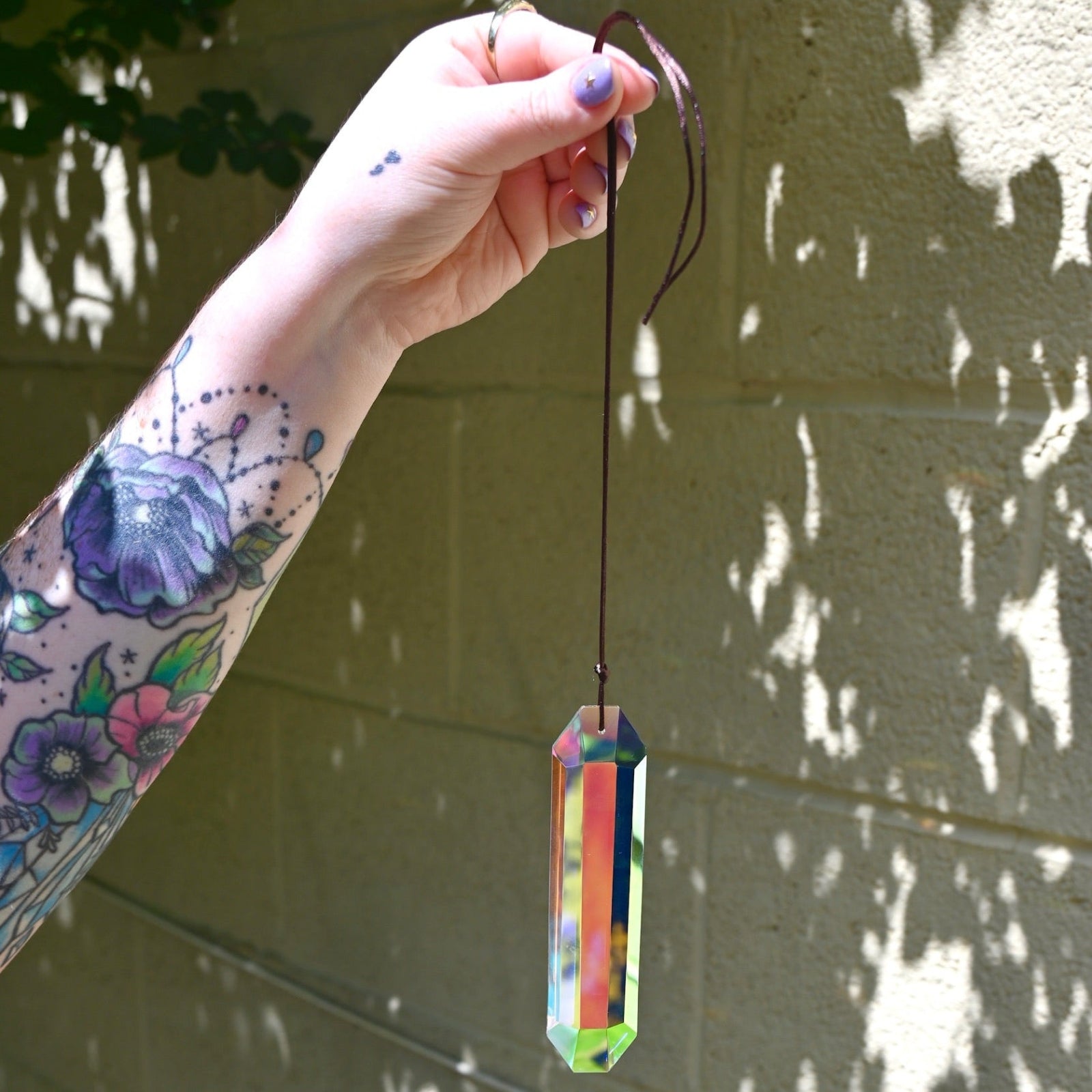 Someone holding the Prism Suncatcher in front of a cream-colored brick wall.