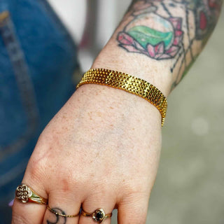 Close-up of vintage-inspired gold mesh bracelet on tattooed wrist