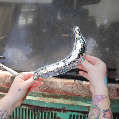Person holding a disco ball shaped like a banana against a rusty metal surface.