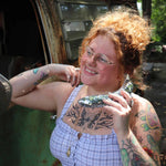 Person with tattoos holding a metallic object, standing next to a vehicle.