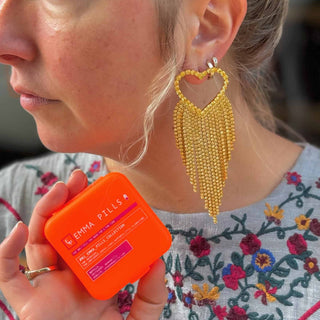 Emma Pills Do Not Party Without Them heart-shaped disco earrings with gold and crystal fringe worn by model holding earring case