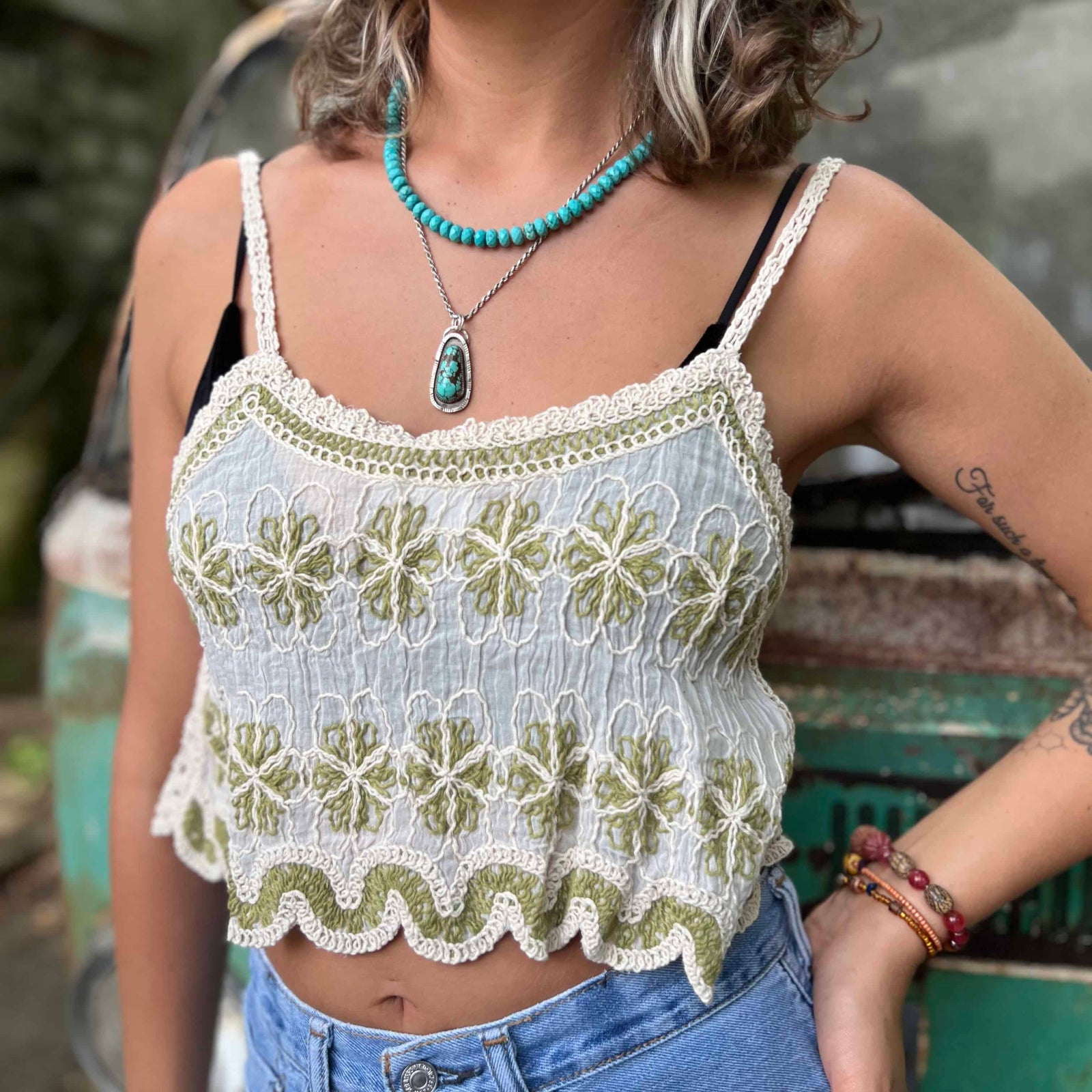Model wearing embroidered cotton-linen crop tank top with green floral detail and scalloped hem