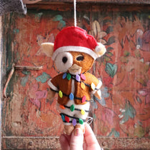 Felt teddy bear ornament with a Santa hat and Christmas lights against a rustic wooden background.