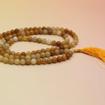 Golden Healer 108 Mala Necklace on pink and orange background