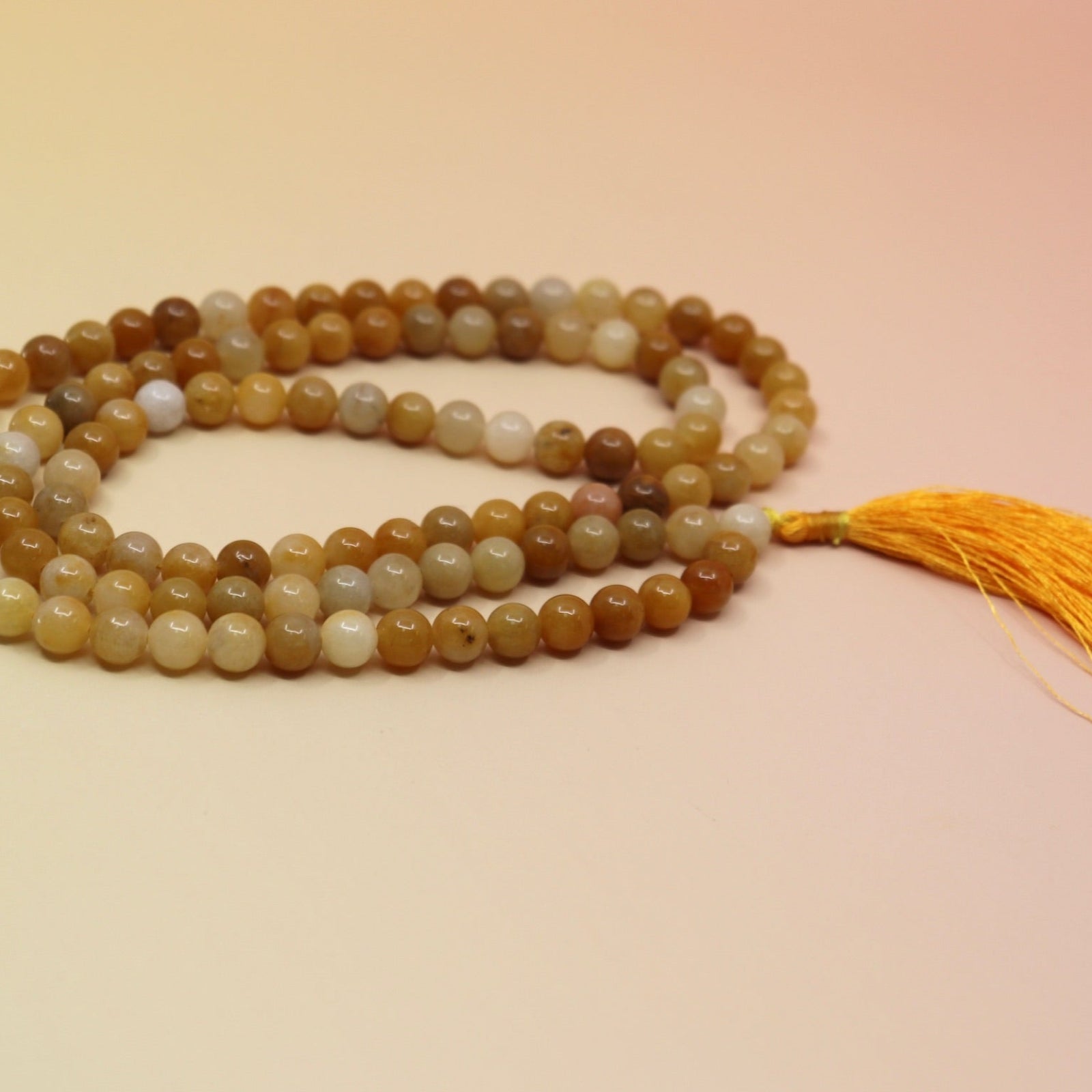 Golden Healer 108 Mala Necklace on pink and orange background