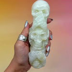 Hand holding green onyx skull stack with silver nails in front of a gradient background