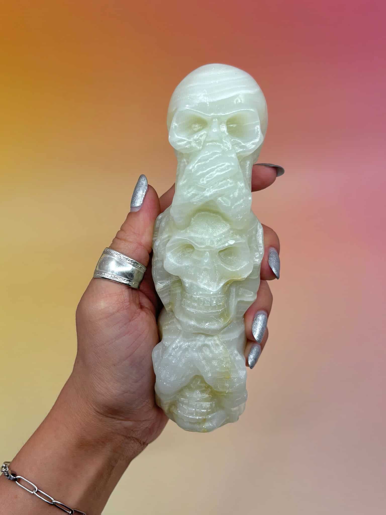 Hand holding green onyx skull stack with silver nails in front of a gradient background