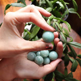 Hand holding a collection of green aventurine balls with a blurred plant background