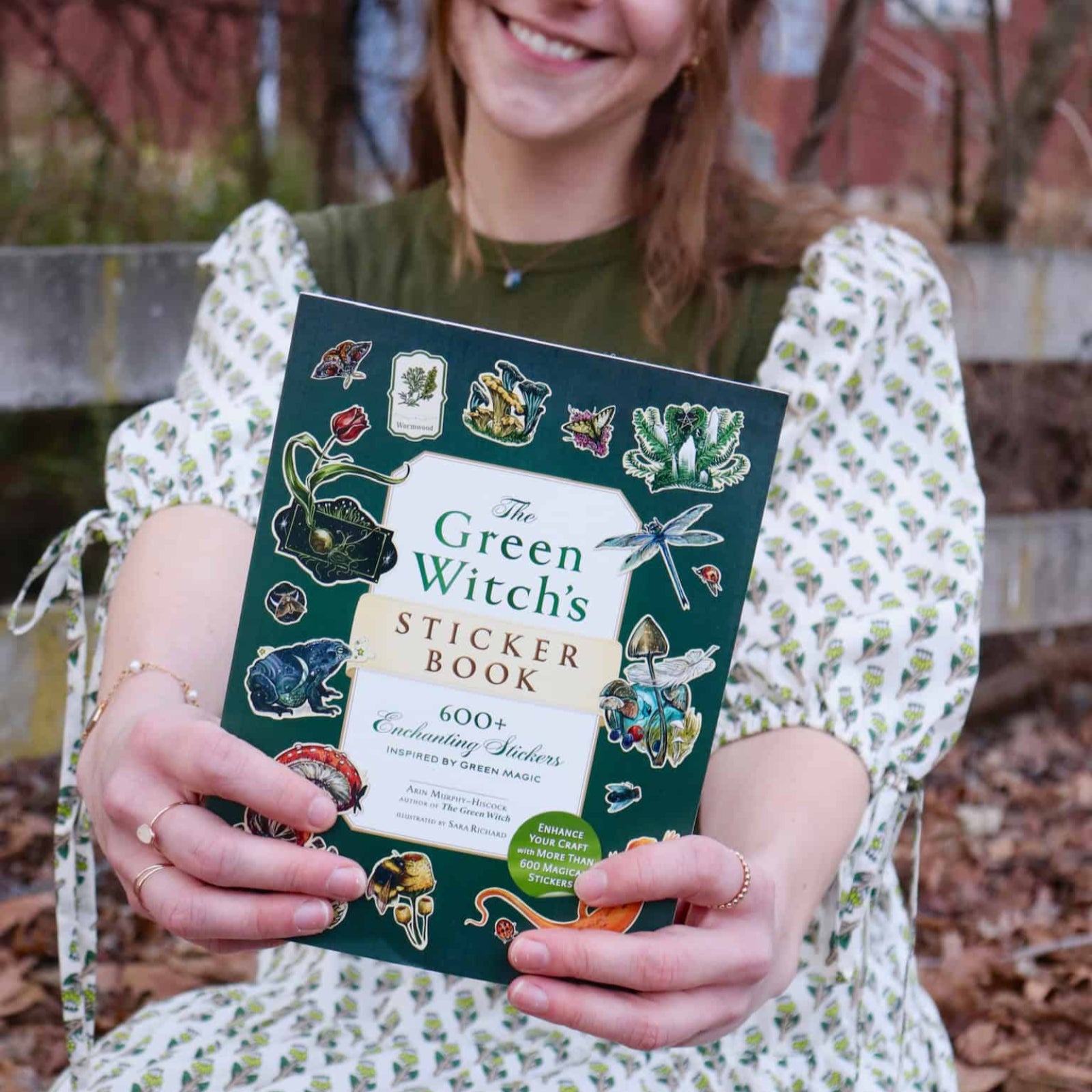 A woman holding the Green Witch's Sticker Book by Arin Murphy-Hiscock.