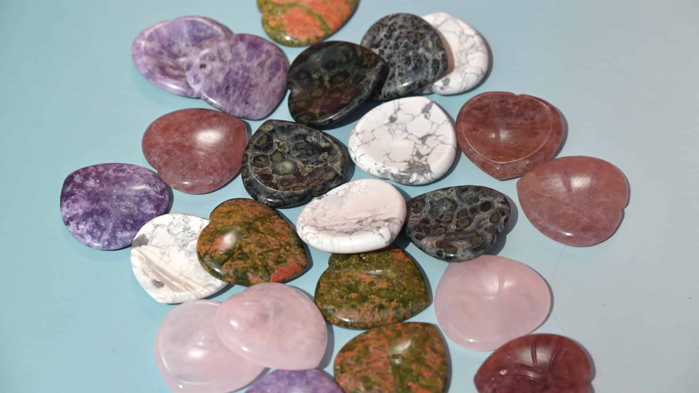 A collection of heart-shaped worry stones in various colors and patterns, displayed on a blue surface.