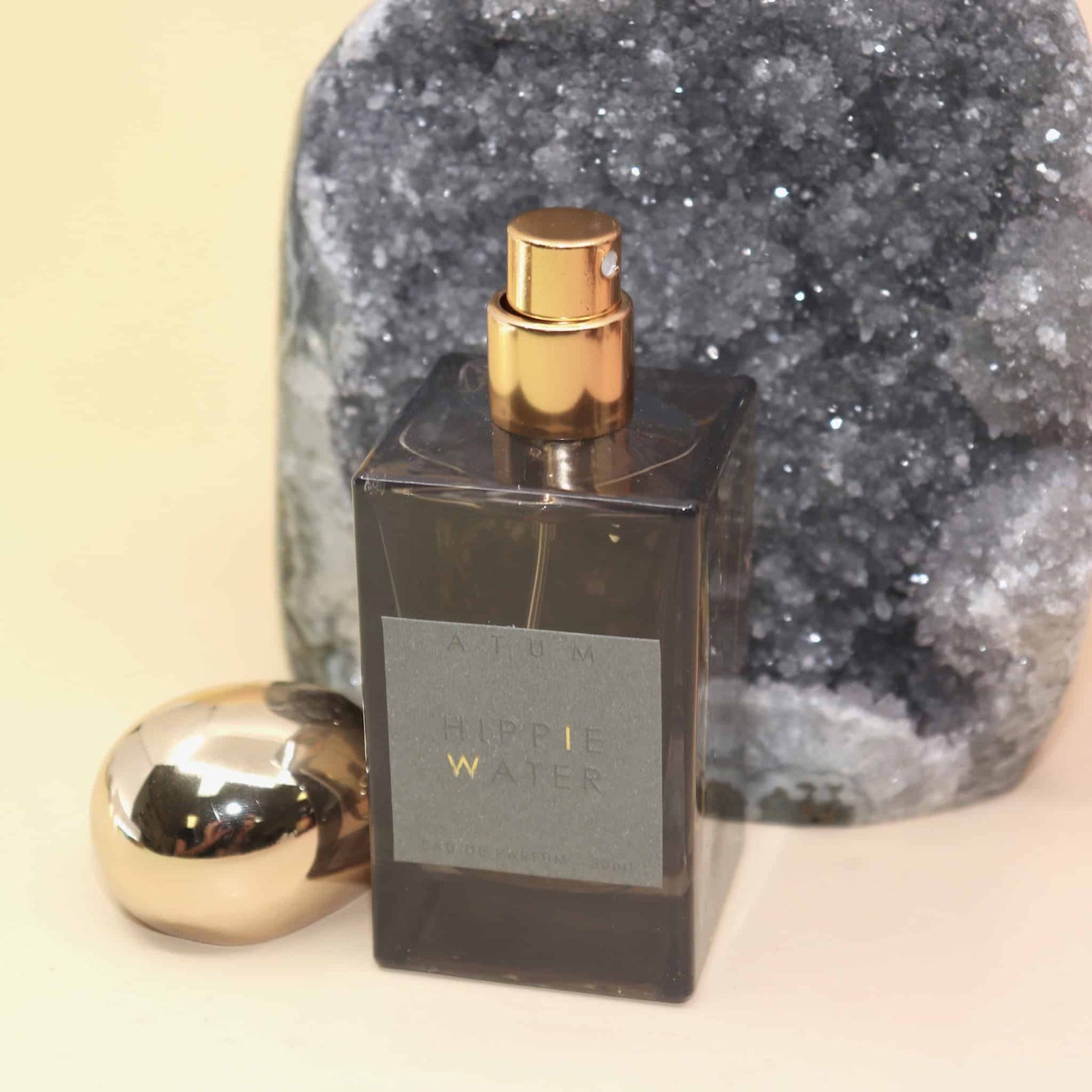 Hippie Water by Atum Perfume bottle with gold cap and dark glass container against a textured stone background