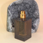 Dark glass Hippie Water Atum perfume bottle with gold cap on a beige background