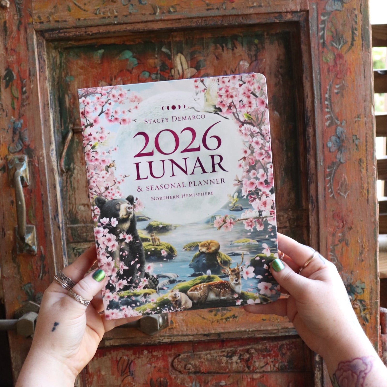 Someone holding the 2026 Lunar and Seasonal Northern Hemisphere Planner Calendar in front of a wooden door.