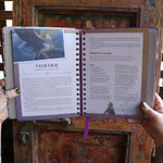 Someone holding the 2026 Lunar and Seasonal Northern Hemisphere Planner Calendar open in front of a wooden door, showing off the pages.