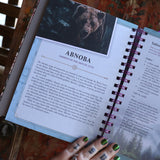 Someone holding the 2026 Lunar and Seasonal Northern Hemisphere Planner Calendar open in front of a wooden door, showing off the pages.