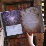 Someone holding the 2026 Lunar and Seasonal Northern Hemisphere Planner Calendar open in front of a wooden door, showing off the pages.