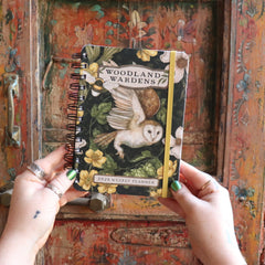 Someone holding the Woodland Wardens 2026 Weekly Planner in front of a door.