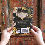 Someone holding the Woodland Wardens 2026 Weekly Planner in front of a door, showing off the back.