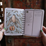 Someone holding the Woodland Wardens 2026 Weekly Planner in front of a door, showing off the pages.